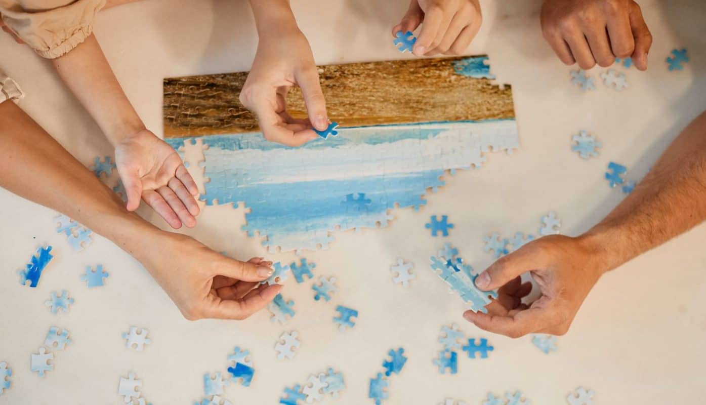 several hands of people helping to finish a jigsaw puzzle