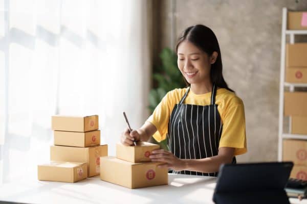 women with apron on smiling while signing form on top of boxes at a desk