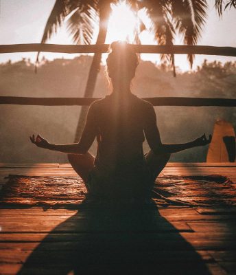 women in yoga pose facing a sunset