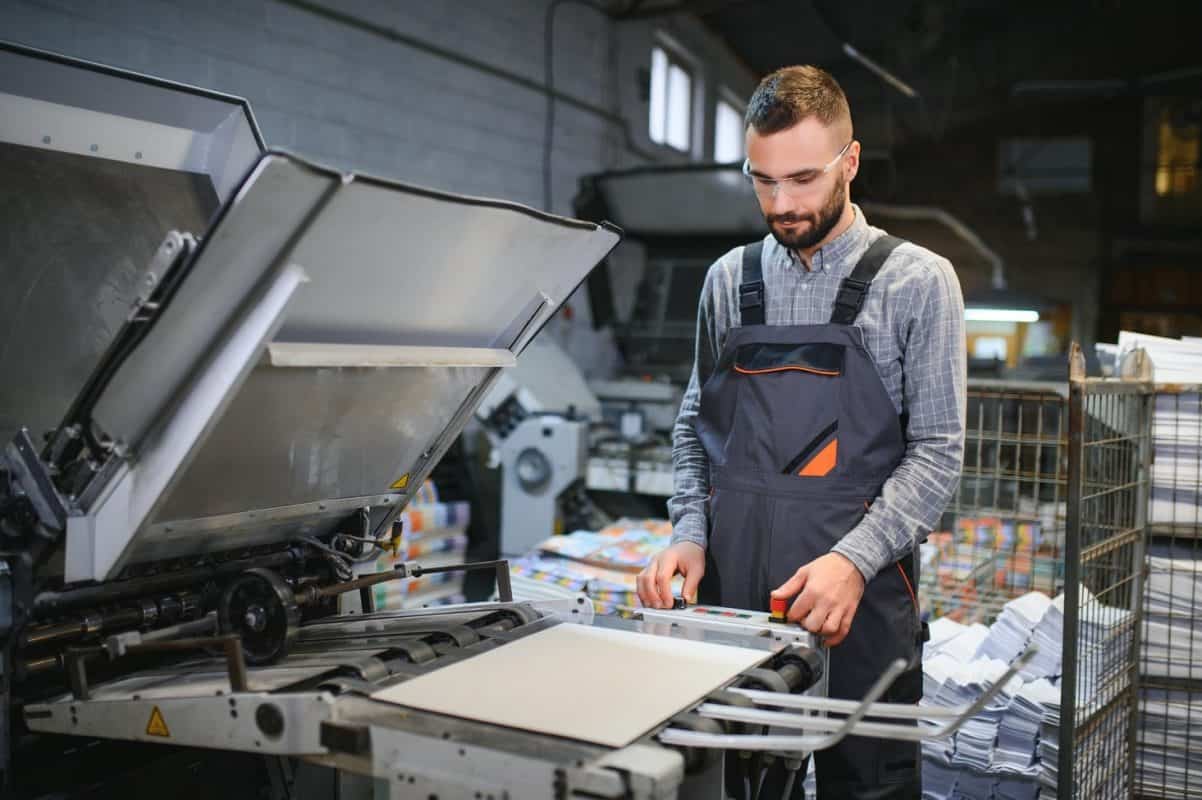 Printing house interior with modern offset print machine and operator in working uniform