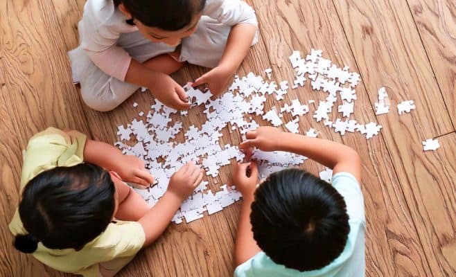 three kids gathered around building a jigsaw puzzle