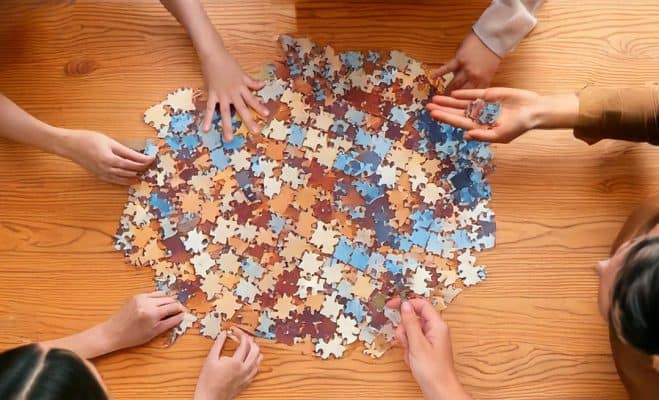 lots of pieces of jigsaw puzzles on the floor with hands reaching for it