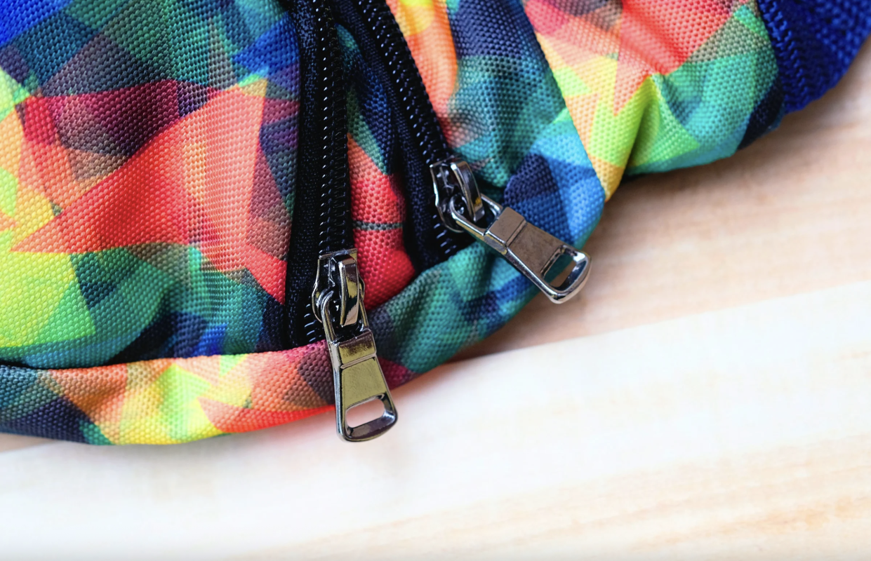 A detailed close-up of a custom fanny pack, showcasing a vibrant, multi-colored print and the high quality construction of its durable double zippers.