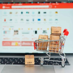 laptop with ecommerce loaded and a miniature toy shopping cart filled with boxes in front of the laptop
